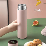 Pink thermos held by a hand on a green surface with figs and bread