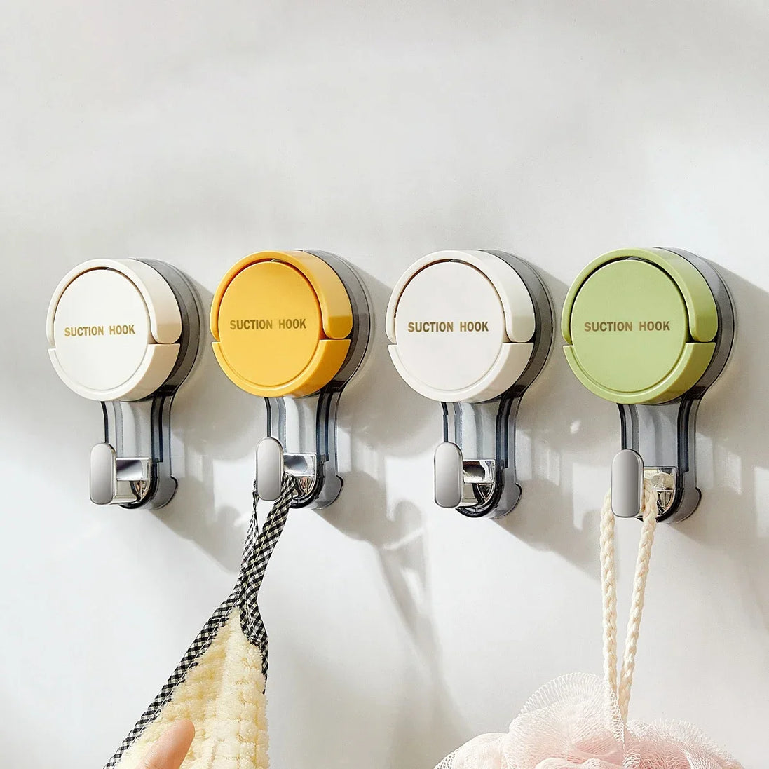 Four suction hooks in different colors on a white wall.