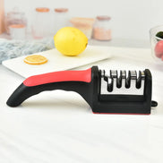 Knife sharpener with a red handle on a white surface, with lemons and a cutting board in the background.
