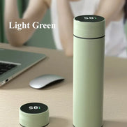 Light green thermos bottle with digital display on a desk with a blurred person and laptop in the background.