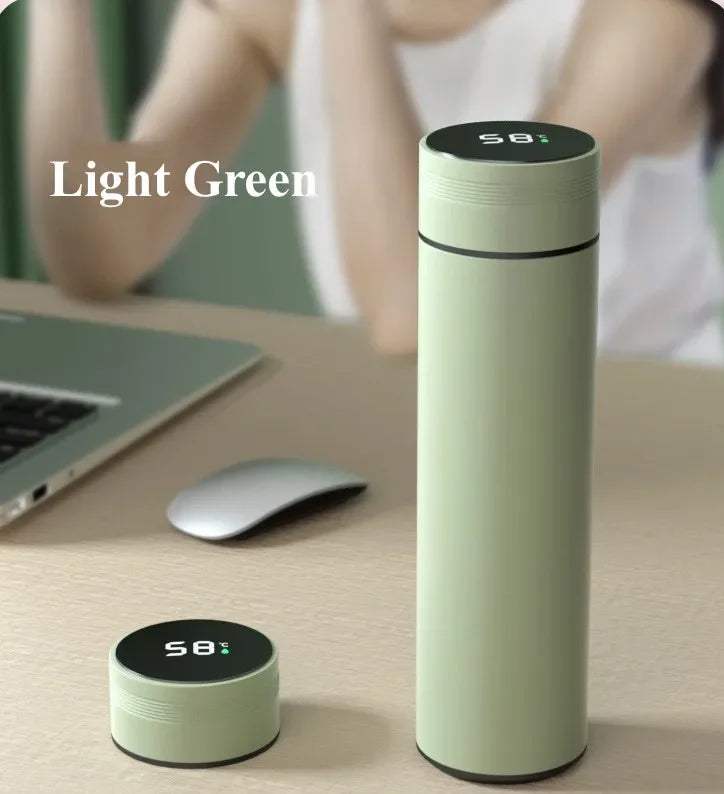 Light green thermos bottle with digital display on a desk with a blurred person and laptop in the background.
