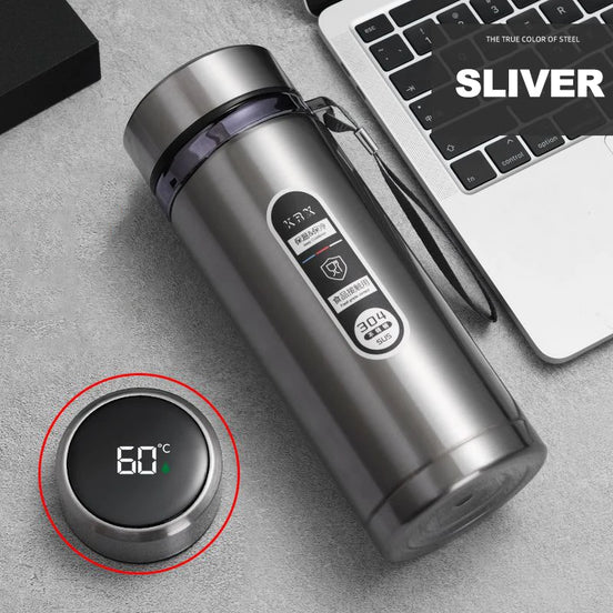 Silver thermos bottle with digital temperature display on a gray surface next to a laptop.