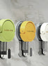 Three suction hooks in green, yellow, and white on a marble wall.