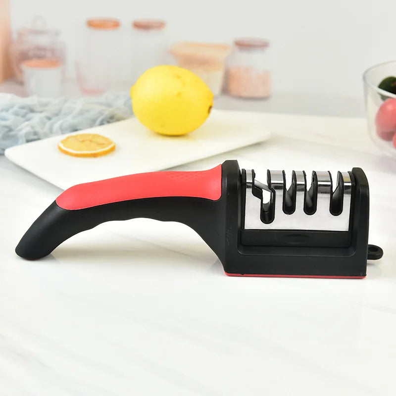 Knife sharpener with a red handle on a white surface, with lemons and a cutting board in the background.