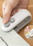 Hand using a small white device to open a snack package on a wooden surface.