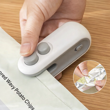 Hand using a small white device to open a snack package on a wooden surface.